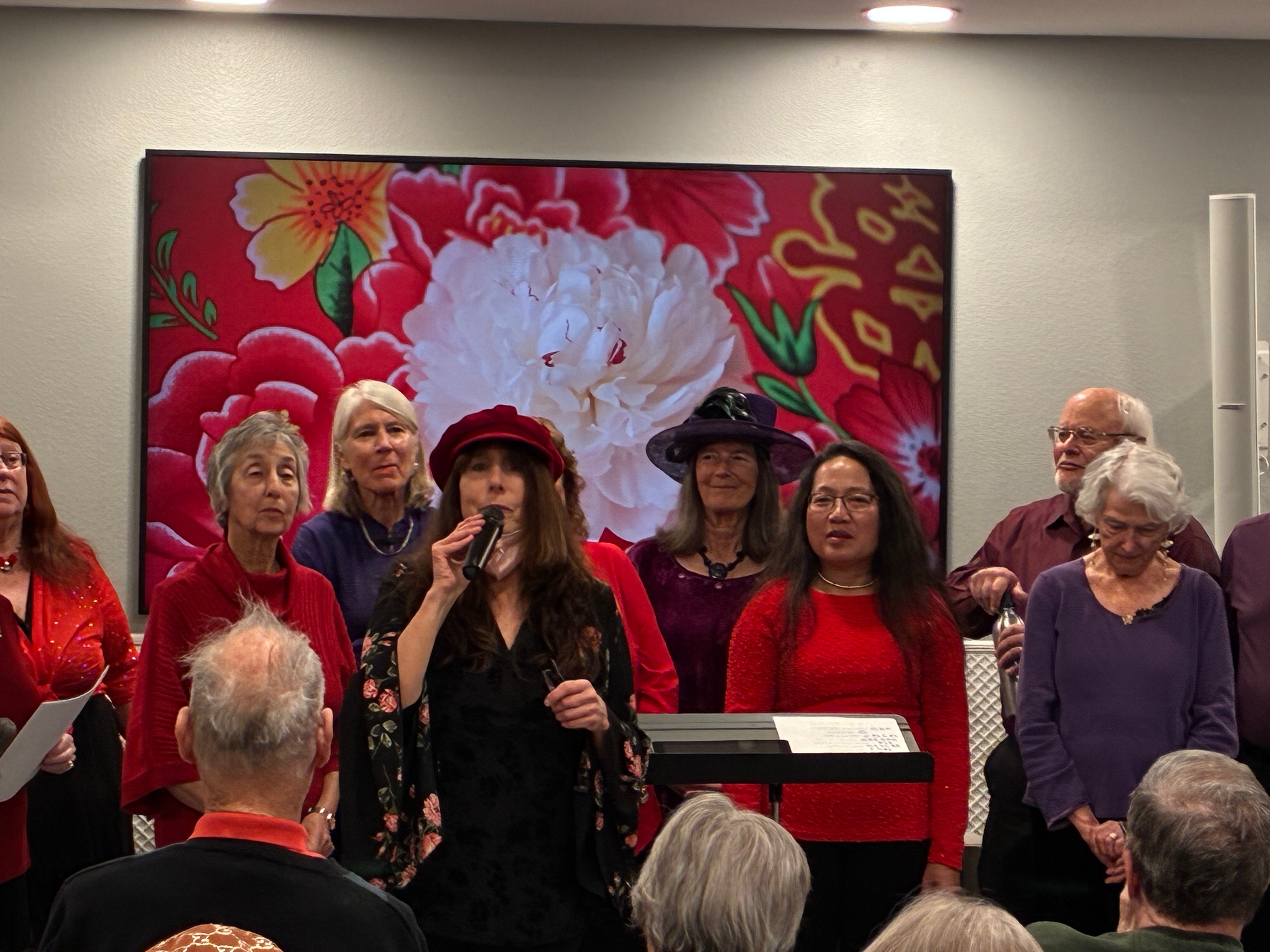 Chorus members in red and purple performing with a microphone in front of a floral backdrop