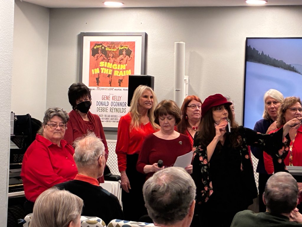 The chorus performing in red attire for an audience in a community hall
