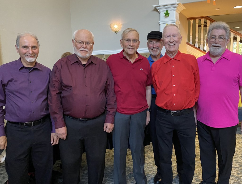 Four chorus members in coordinated purple and red performance shirts
